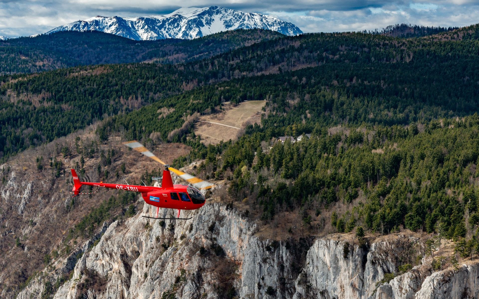 Roter Hubschrauber fliegt über karge Berglandschaft
